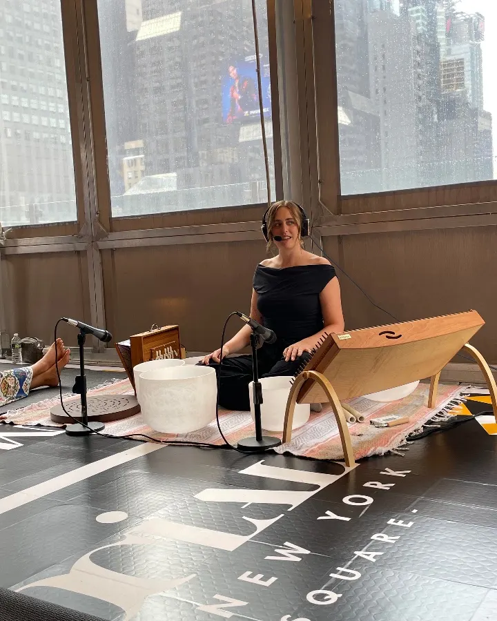 A woman plays musical instruments in a vibrant setting with views of New York City, embodying the energy of Times Square.