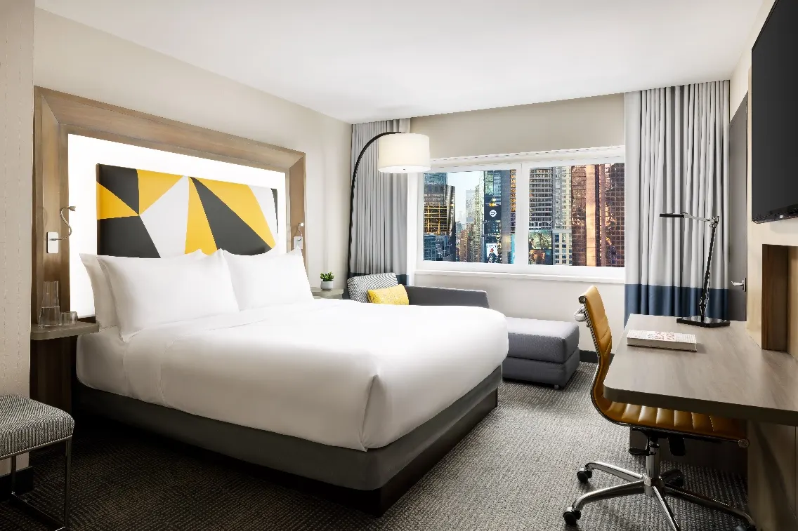 Modern hotel room at M Social Times Square featuring a cozy bed, stylish decor, and large windows with a vibrant city view.