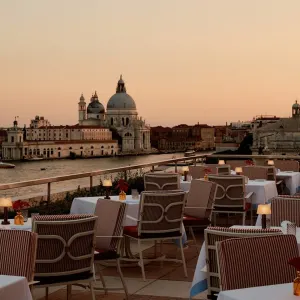 Dining tables set on a terrace with a view of Venice's stunning architecture and bustling waterways at sunset.