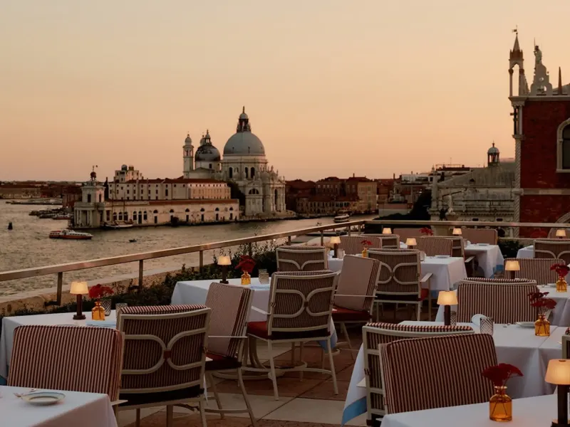 Dining tables set on a terrace with a view of Venice's stunning architecture and bustling waterways at sunset.
