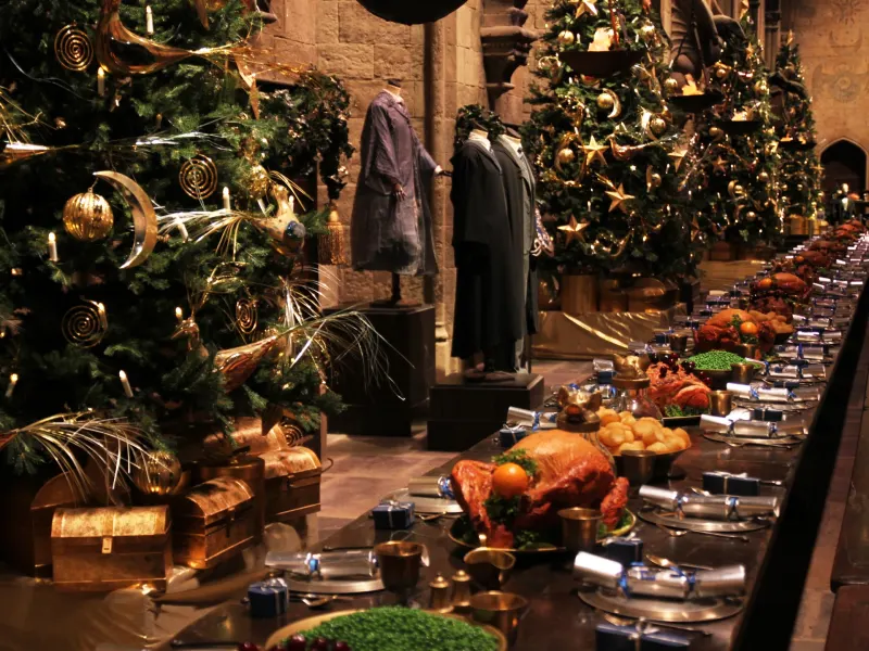 A festive dining hall adorned with decorated Christmas trees and a lavish feast laid out on a long table.