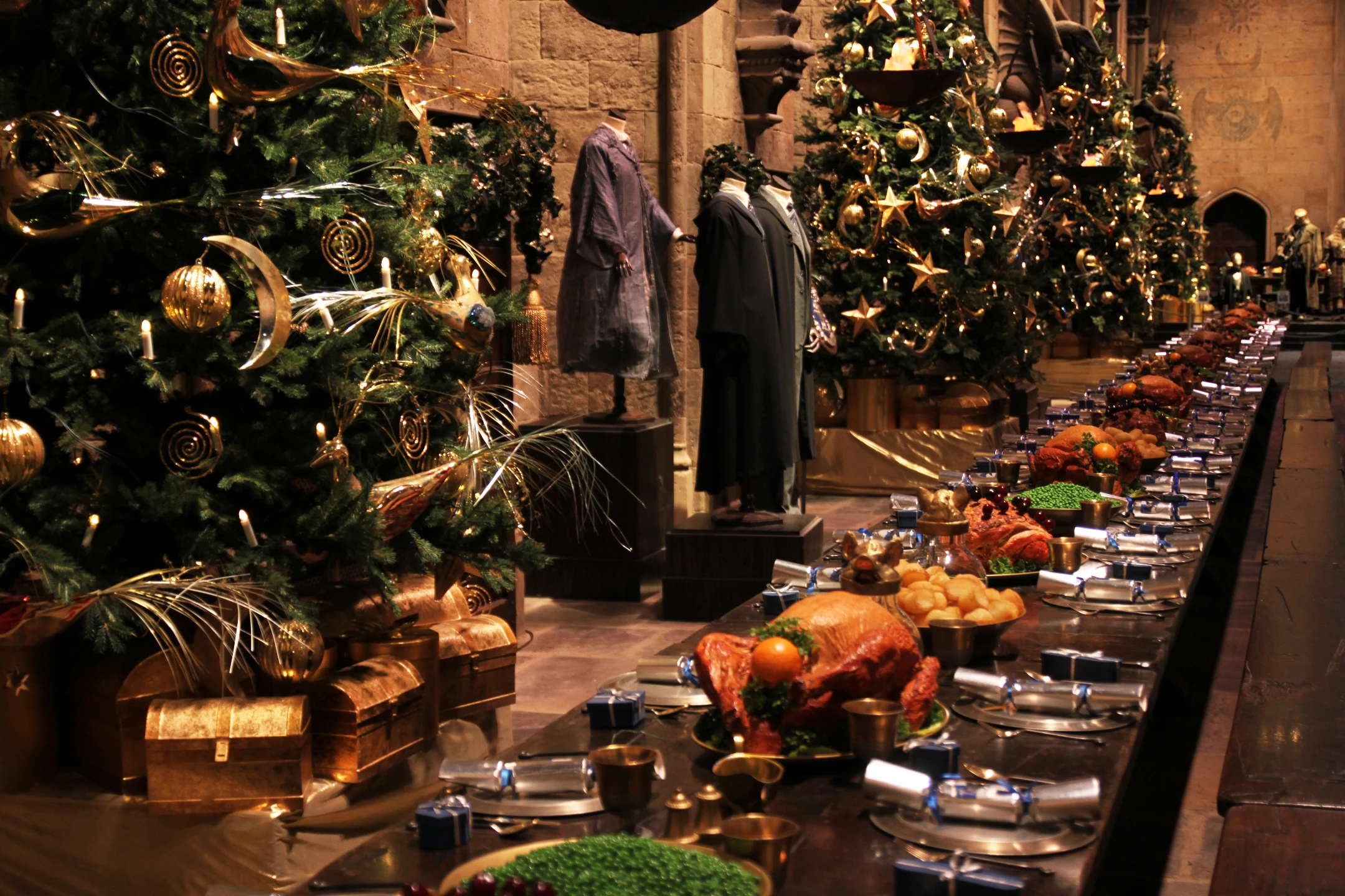 A festive dining hall adorned with decorated Christmas trees and a lavish feast laid out on a long table.