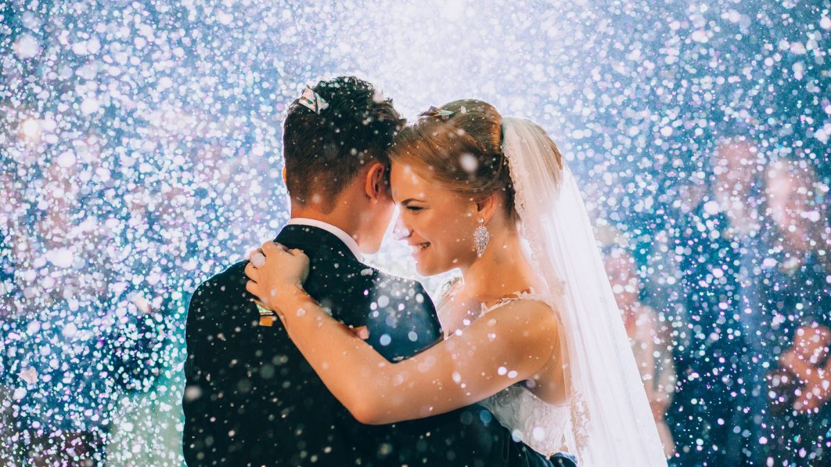 A couple shares an intimate moment during their wedding celebration, surrounded by sparkling confetti or snow.