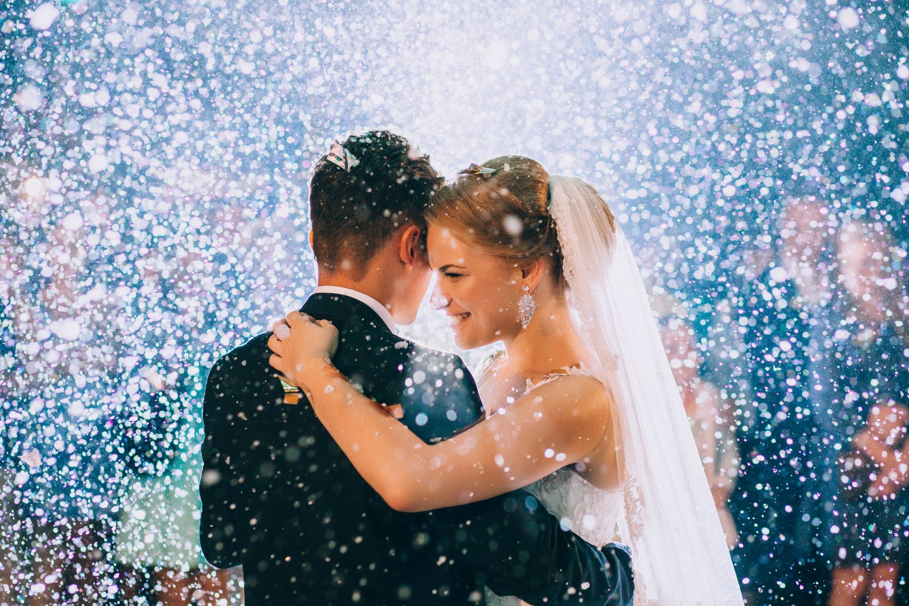 A couple shares an intimate moment during their wedding celebration, surrounded by sparkling confetti or snow.