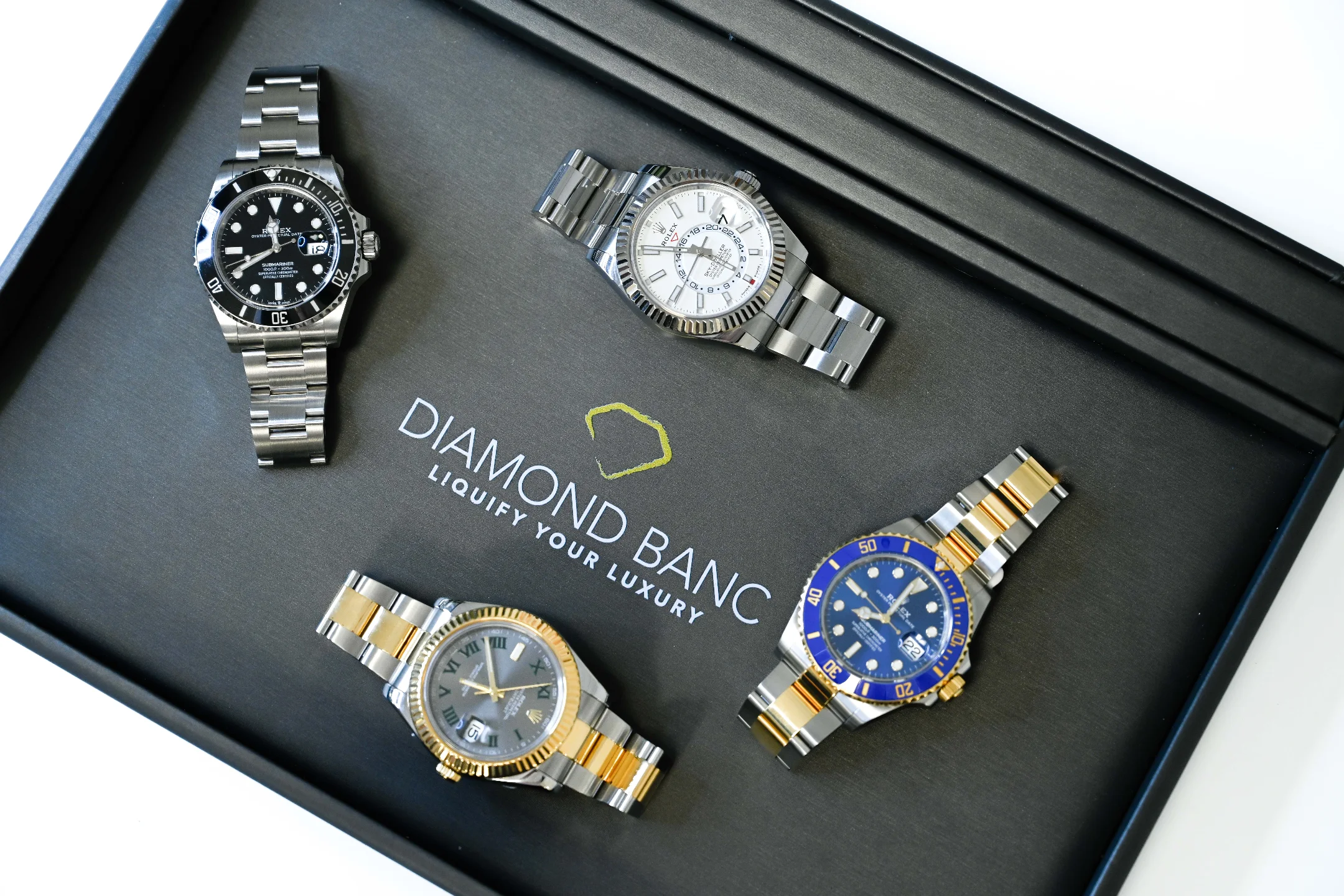 Four luxury Rolex watches displayed in a black box featuring the Diamond Banc logo, highlighting luxury timepieces.