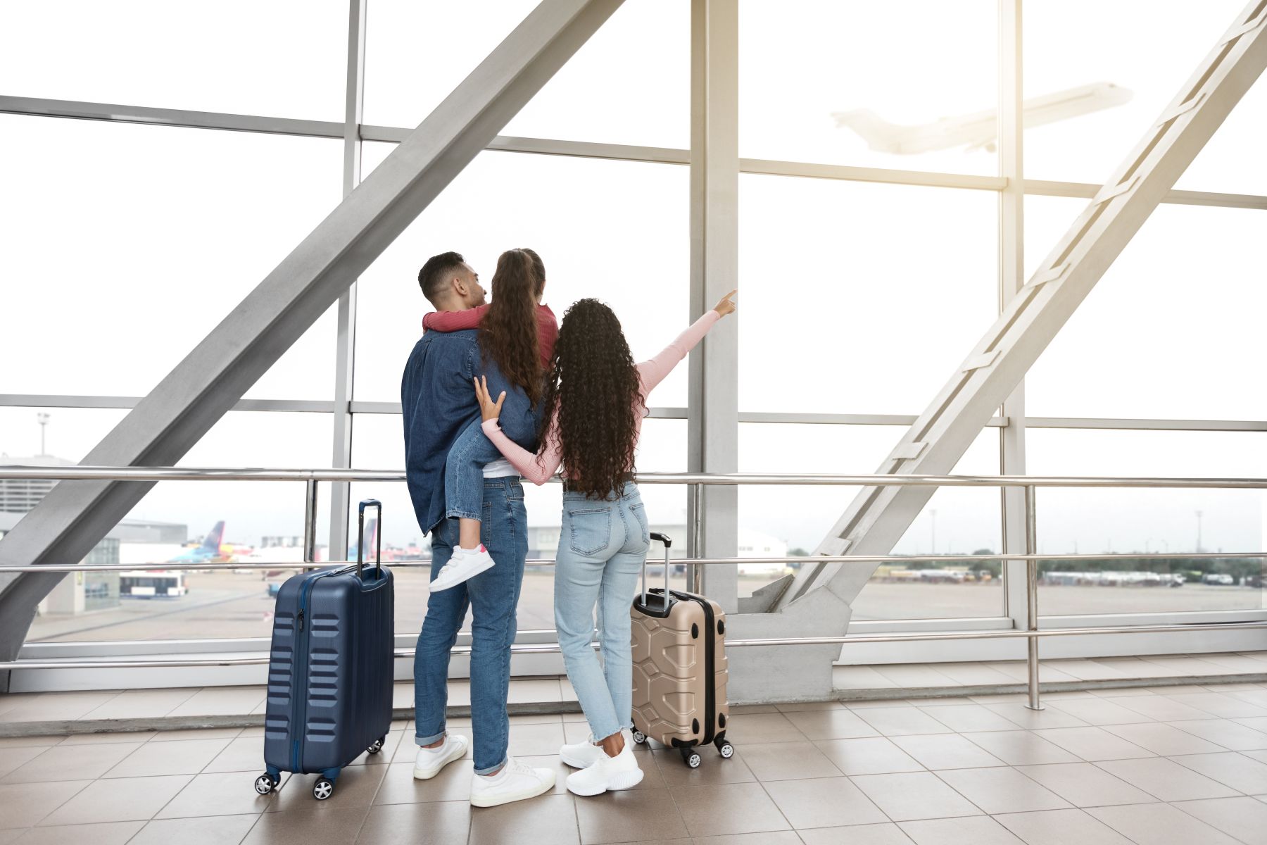 Family at the airport watching an airplane take off, with luggage beside them.