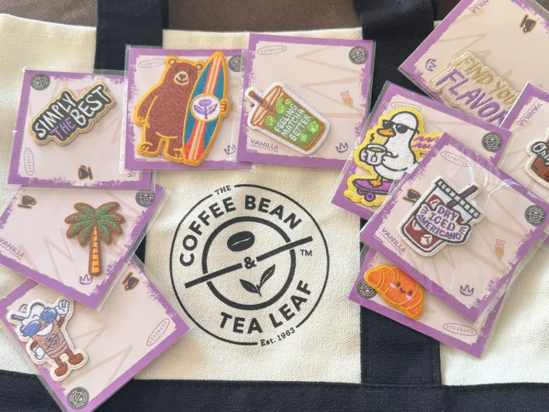 Colorful embroidered patches featuring coffee and tea themes on a tote bag from The Coffee Bean & Tea Leaf.