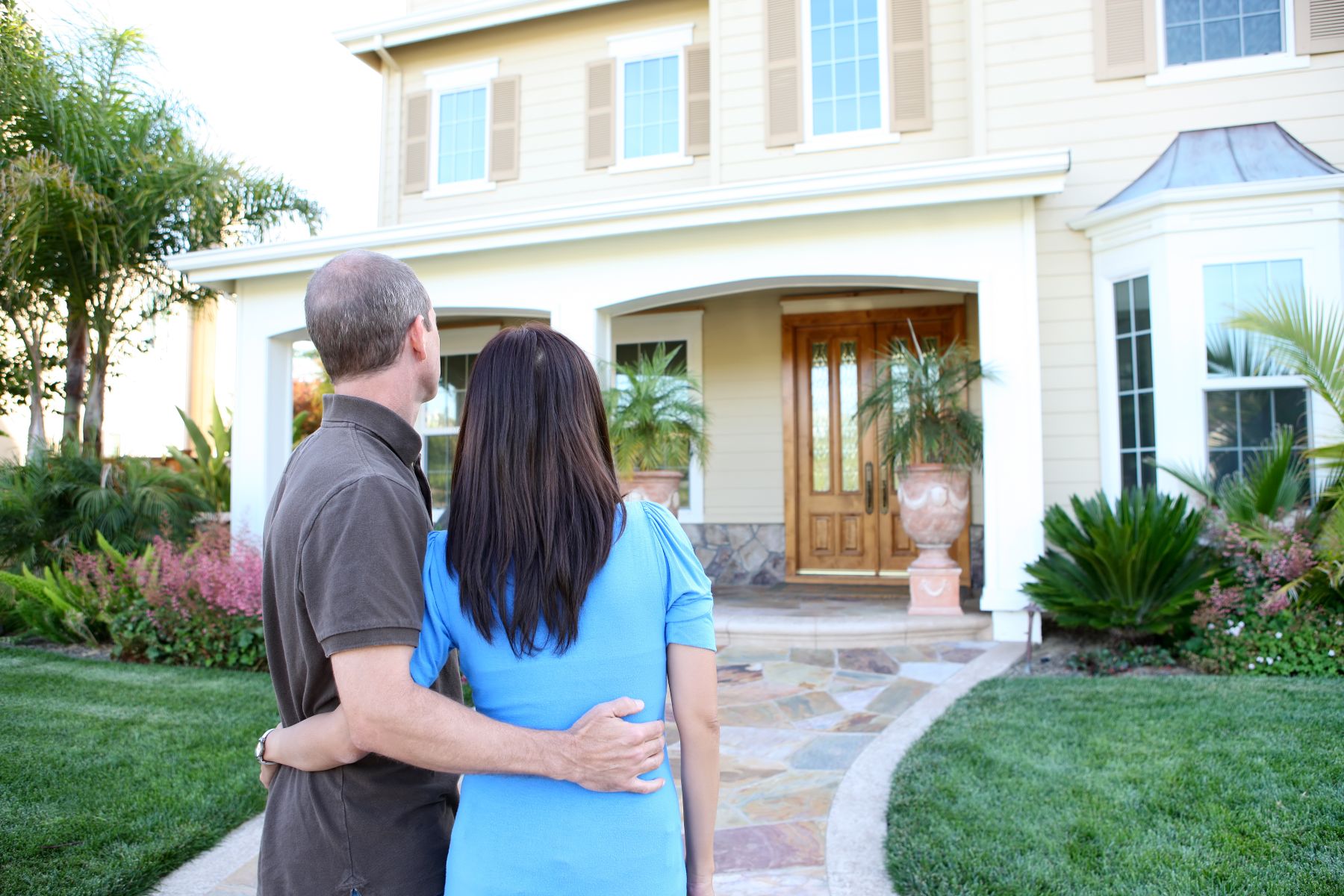 A couple admires their home from the front yard, surrounded by lush landscaping and greenery.