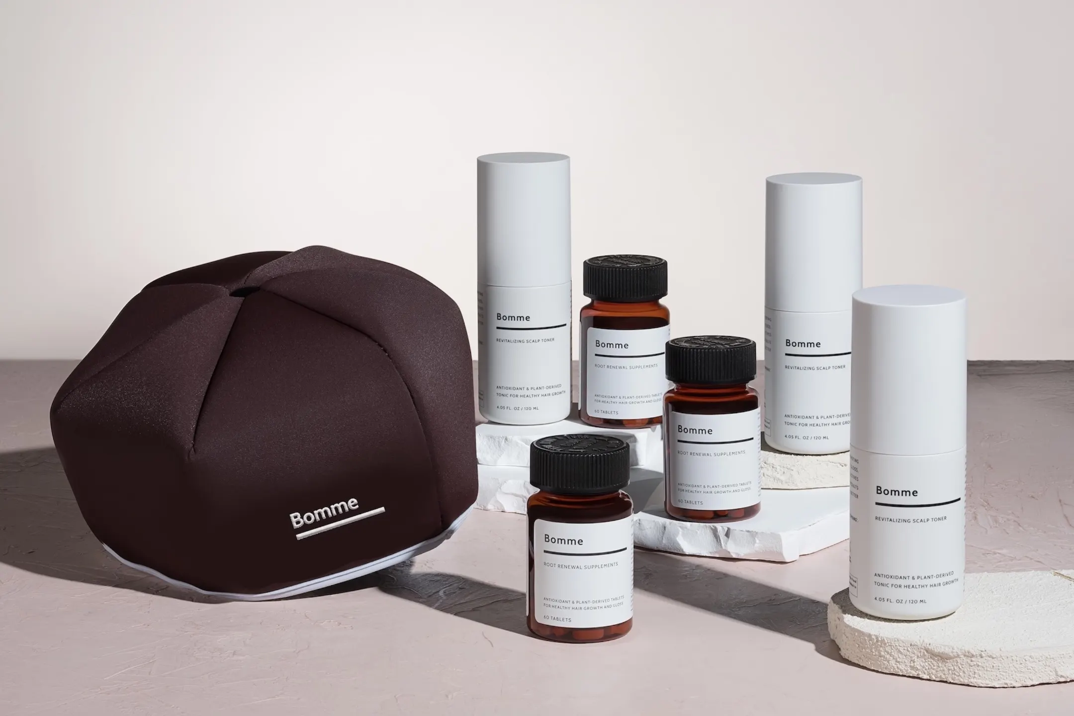 Bomme hair wellness products including scalp toner and dietary supplements displayed on a neutral surface.