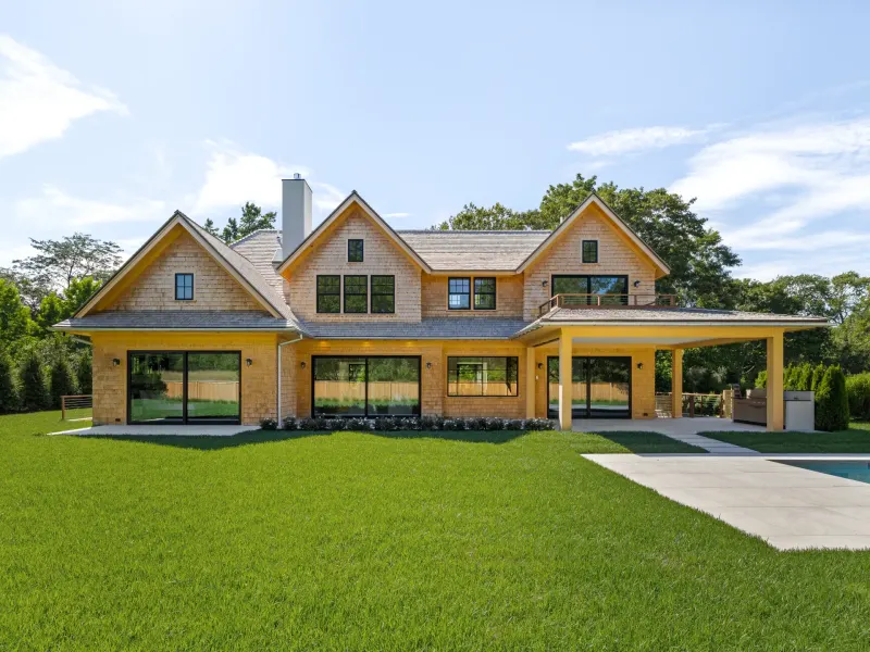 Luxurious East Hampton new build featuring large windows, a spacious yard, and a covered patio near the pool.