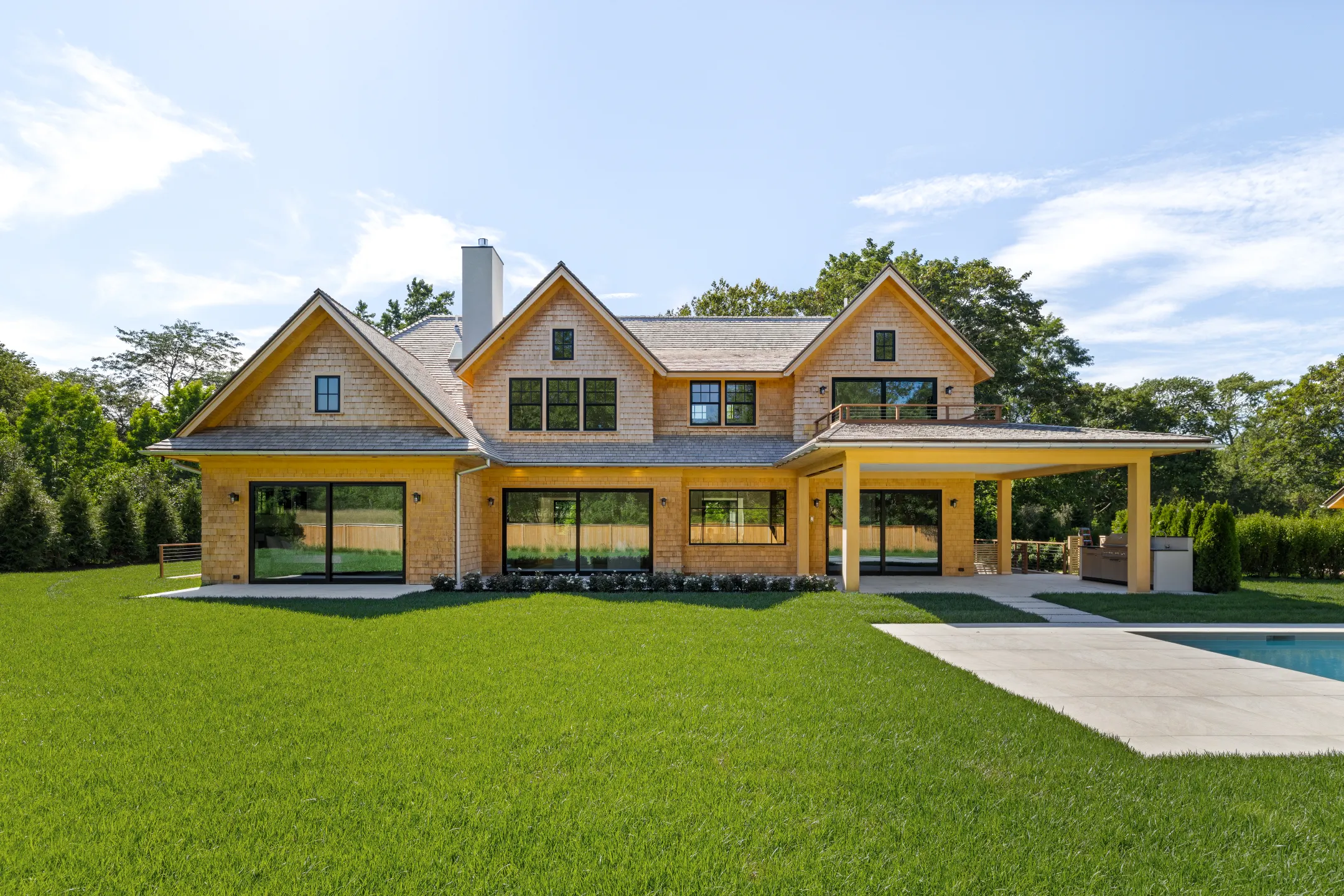 Luxurious East Hampton new build featuring large windows, a spacious yard, and a covered patio near the pool.