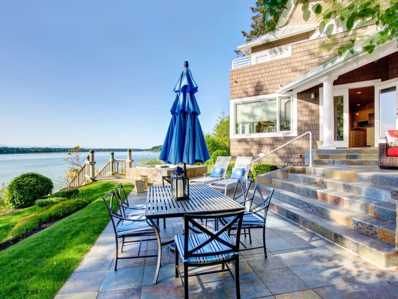 Outdoor patio with a dining table and chairs overlooking a serene body of water and lush greenery.