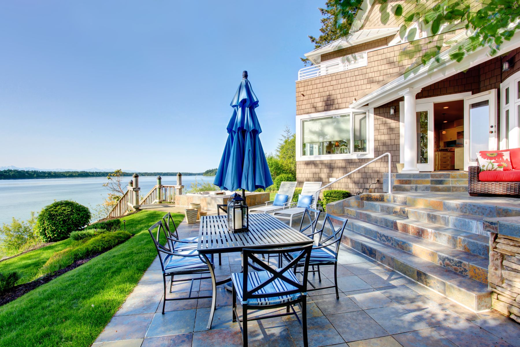 Outdoor patio with a dining table and chairs overlooking a serene body of water and lush greenery.