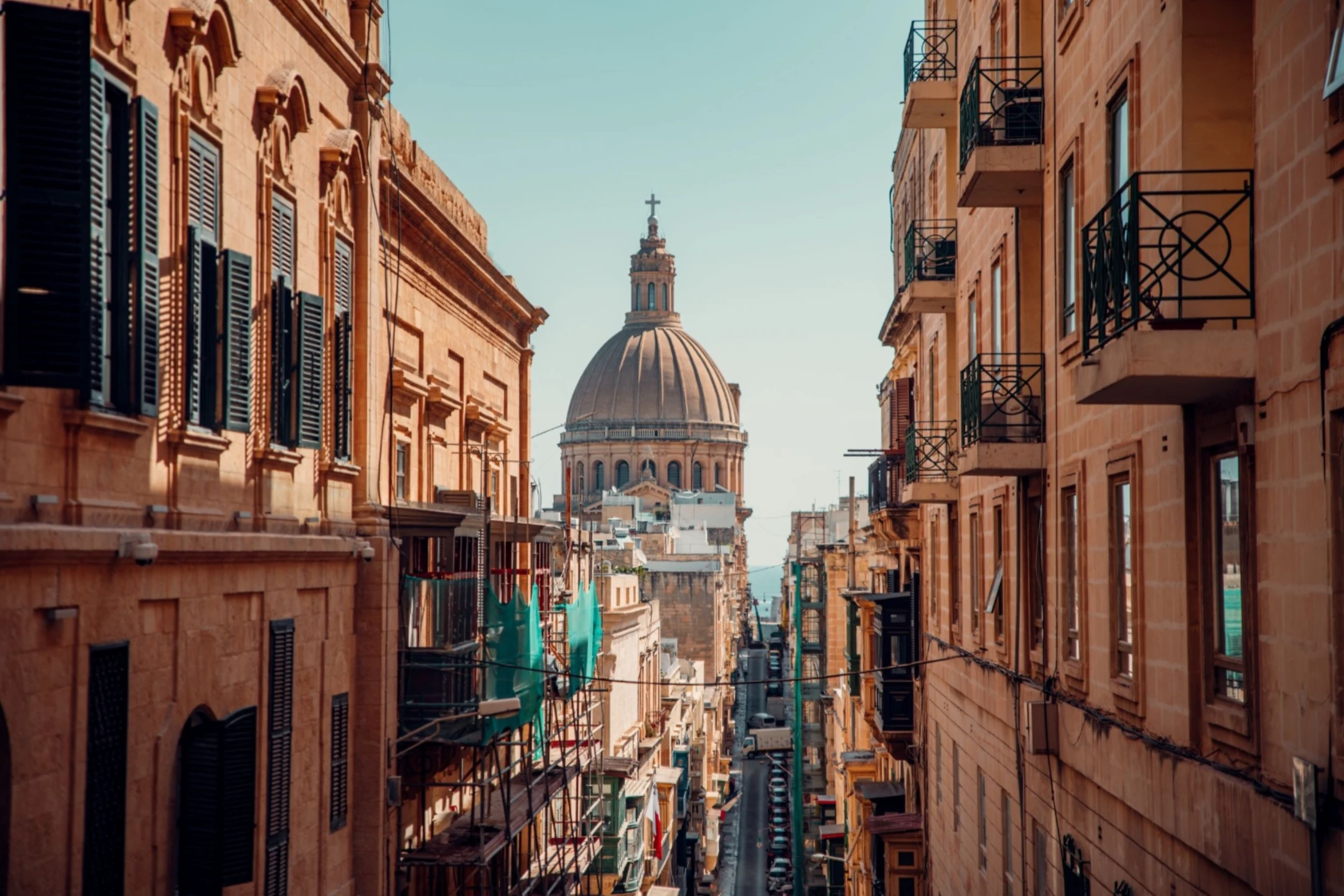 Narrow street in Malta with historic buildings and a prominent dome in the background.