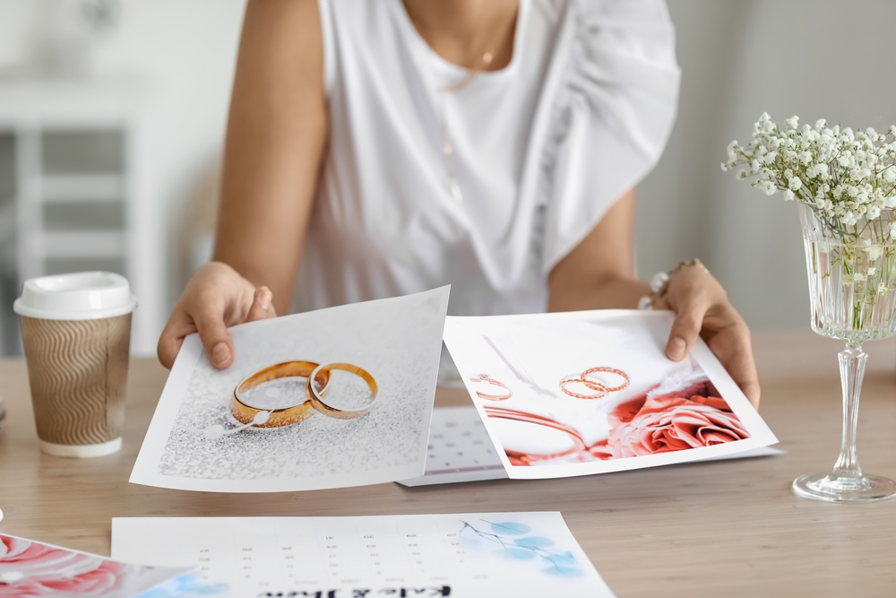 A person examines printed images of wedding rings and floral arrangements while seated at a table with a coffee cup.