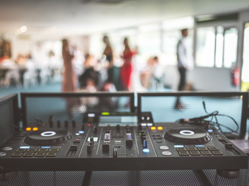 A DJ mixer is set up in a venue with guests socializing in the background, emphasizing the importance of professional AV integration.