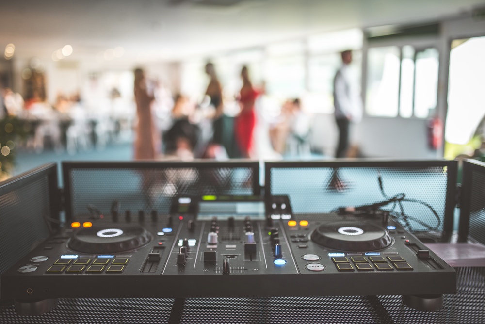 A DJ mixer is set up in a venue with guests socializing in the background, emphasizing the importance of professional AV integration.