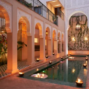 A serene courtyard in Marrakech at night, featuring arched architecture, a reflecting pool, and candles illuminating the space.