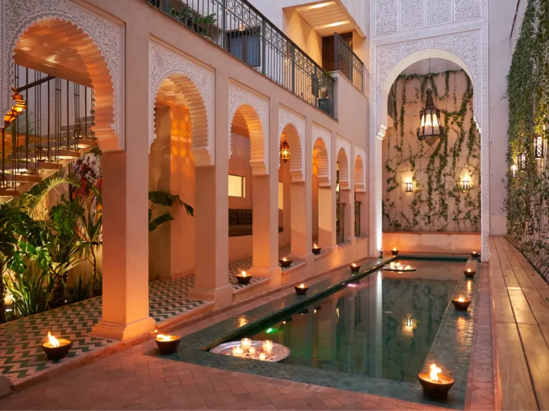A serene courtyard in Marrakech at night, featuring arched architecture, a reflecting pool, and candles illuminating the space.