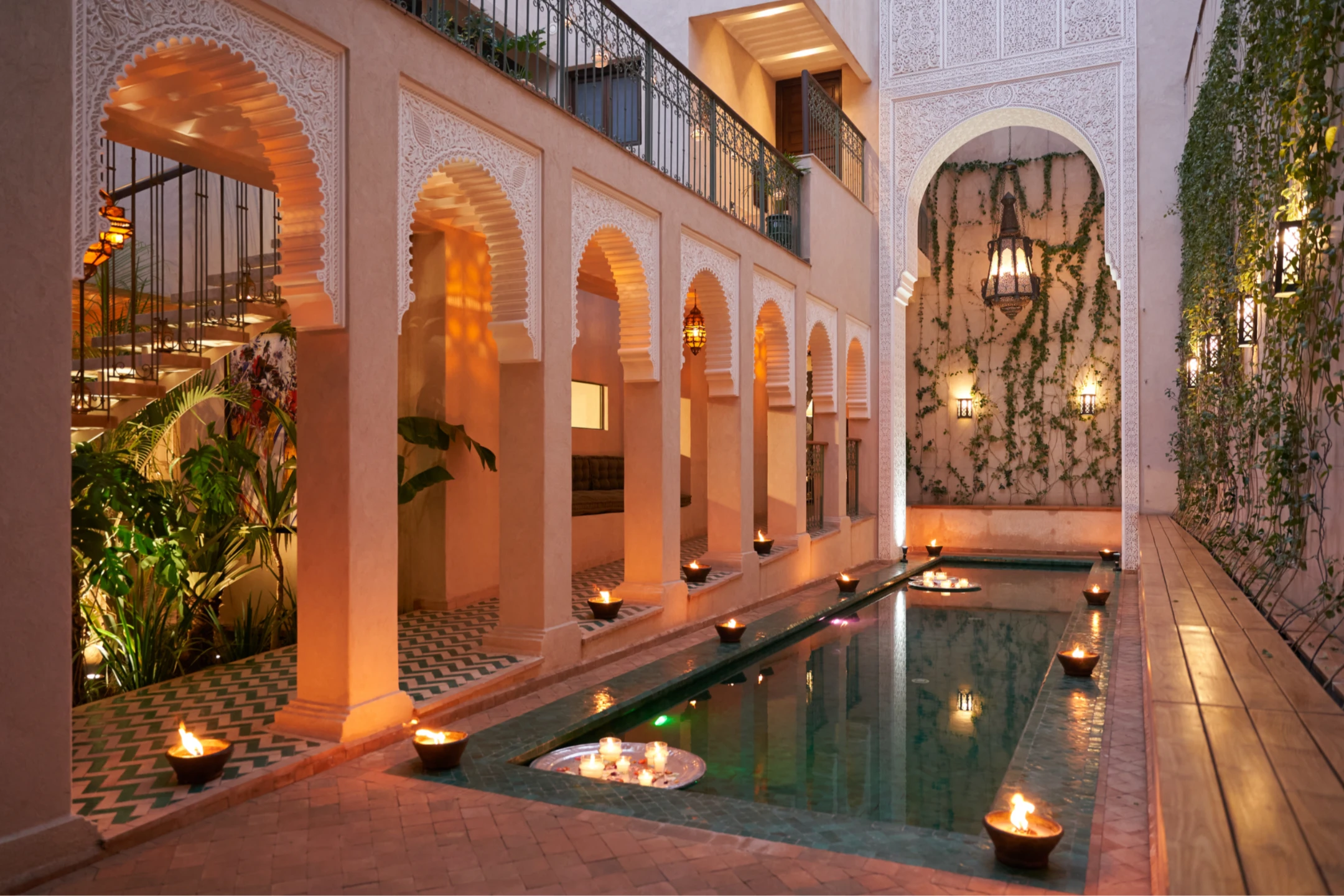 A serene courtyard in Marrakech at night, featuring arched architecture, a reflecting pool, and candles illuminating the space.