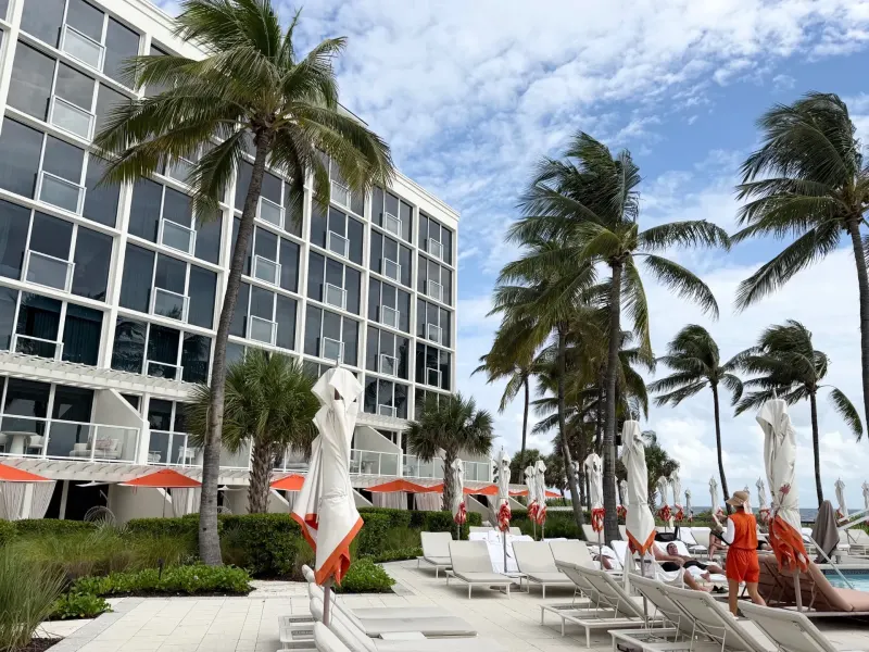 Palm trees and lounge chairs line the poolside at The Boca Raton, with guests enjoying the sunny day and modern architecture in view.