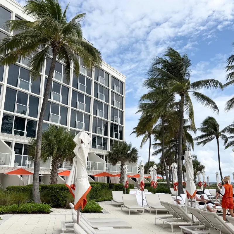 Palm trees and lounge chairs line the poolside at The Boca Raton, with guests enjoying the sunny day and modern architecture in view.