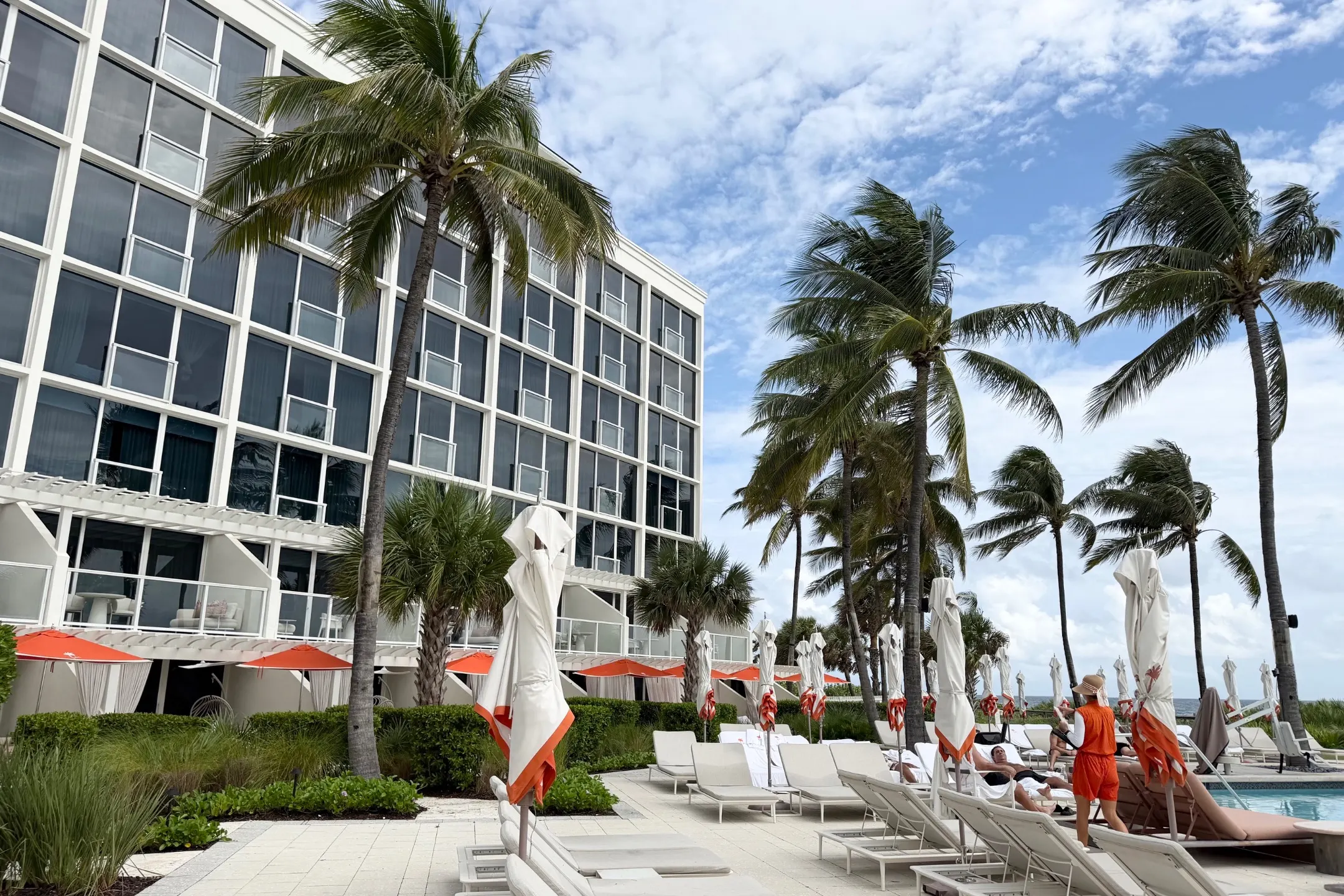 Palm trees and lounge chairs line the poolside at The Boca Raton, with guests enjoying the sunny day and modern architecture in view.