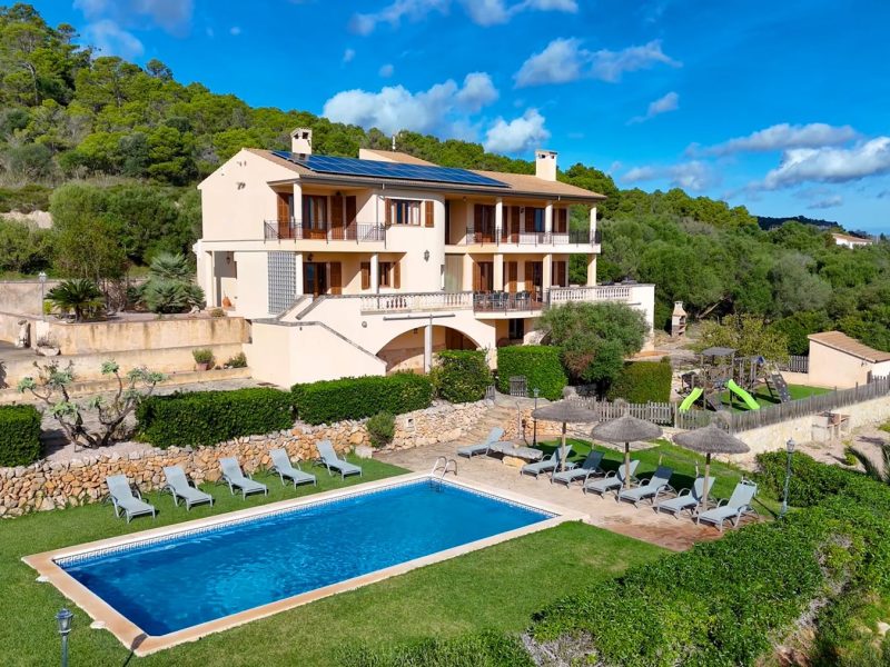 Spacious villa surrounded by greenery, featuring a blue pool and sun loungers, ideal for travelers seeking privacy and relaxation.