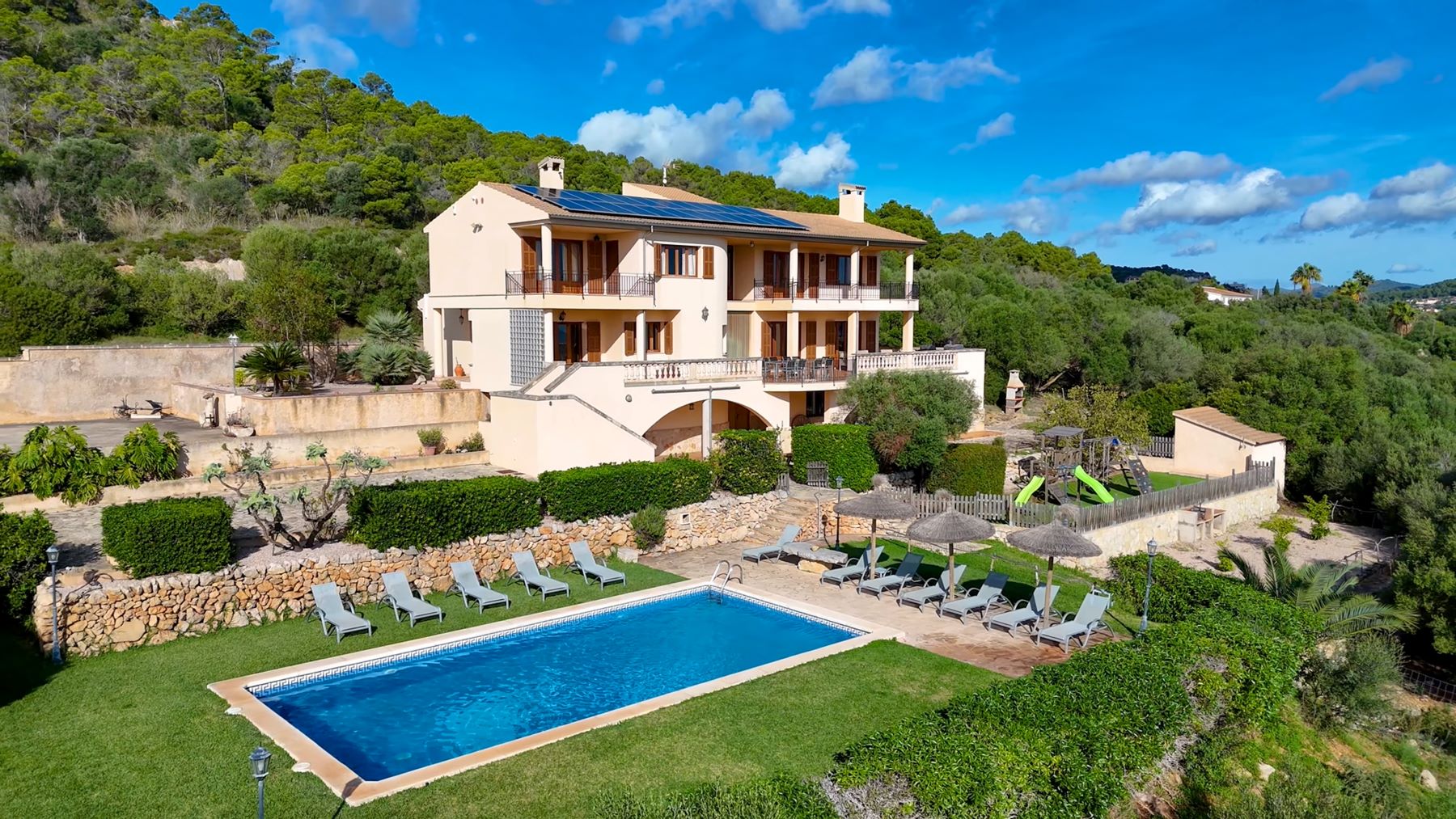 Spacious villa surrounded by greenery, featuring a blue pool and sun loungers, ideal for travelers seeking privacy and relaxation.