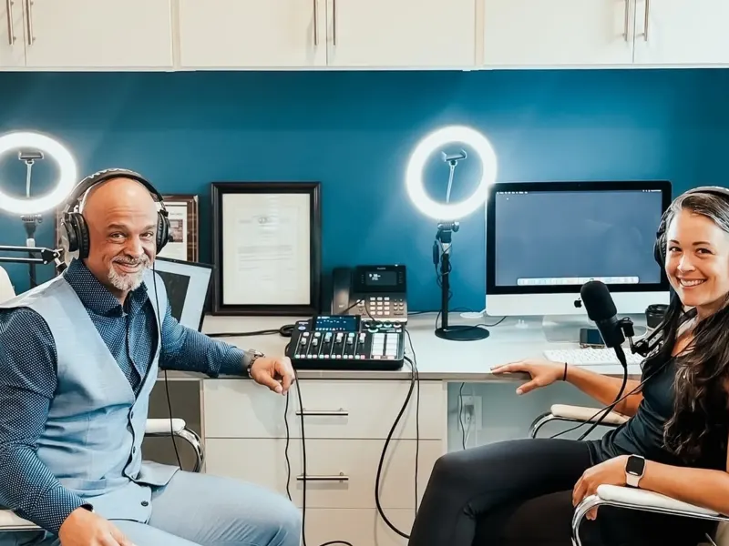 Two podcasters seated at a desk with headphones, discussing topics related to health and finances, in a modern studio setup.