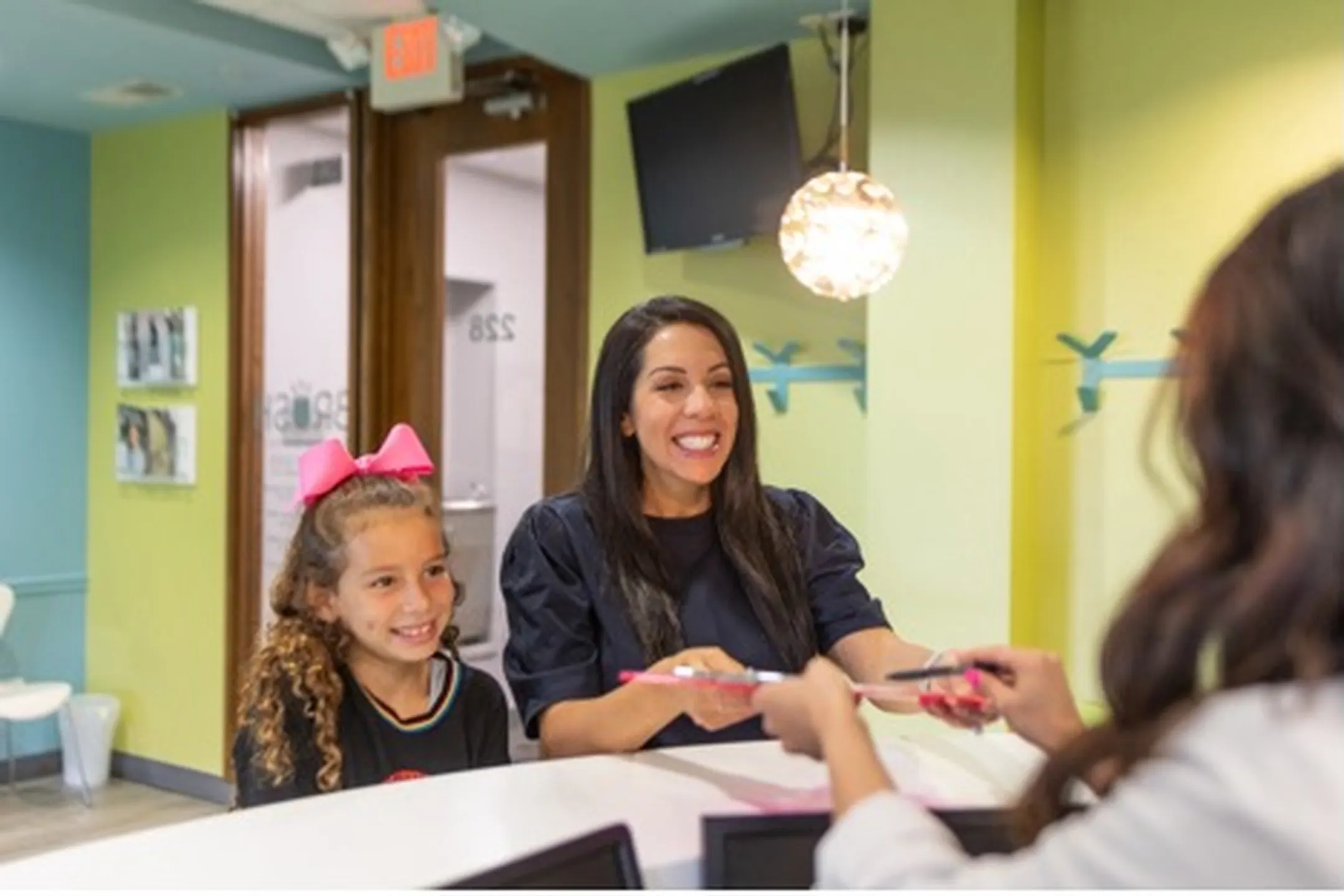 Smiling mother and daughter at a dental office reception, engaging with staff and discussing dental care.