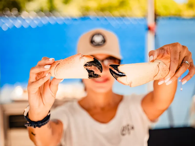 Person holding two large crab claws against a blue background at the South Beach Seafood Festival.