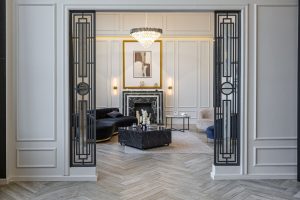 Elegant living room featuring a modern chandelier, marble fireplace, and stylish furniture framed by decorative doors.