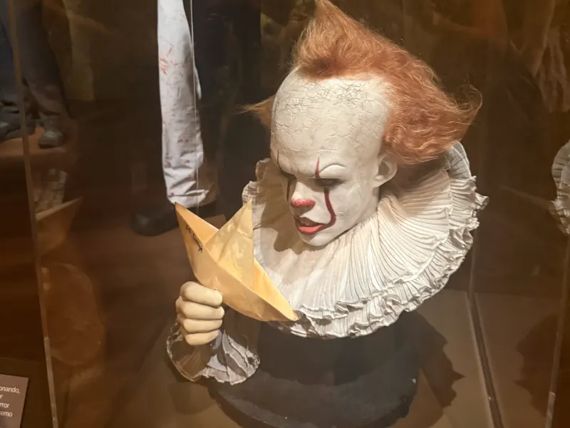 Clown figure holding a paper boat, featured in a horror exhibition at the Academy Museum.