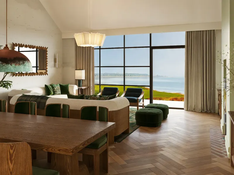Modern great room with a view of the ocean, featuring a wooden dining table, cozy seating, and stylish decor.