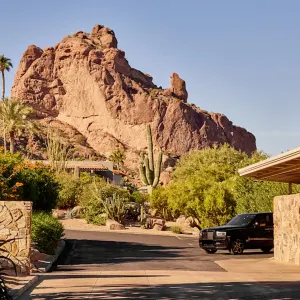 Main entrance of Sanctuary Camelback Mountain Resort surrounded by desert plants and a prominent rock formation in the background.