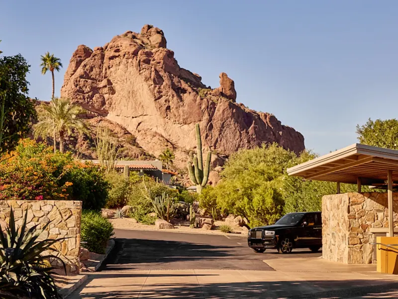 Main entrance of Sanctuary Camelback Mountain Resort surrounded by desert plants and a prominent rock formation in the background.