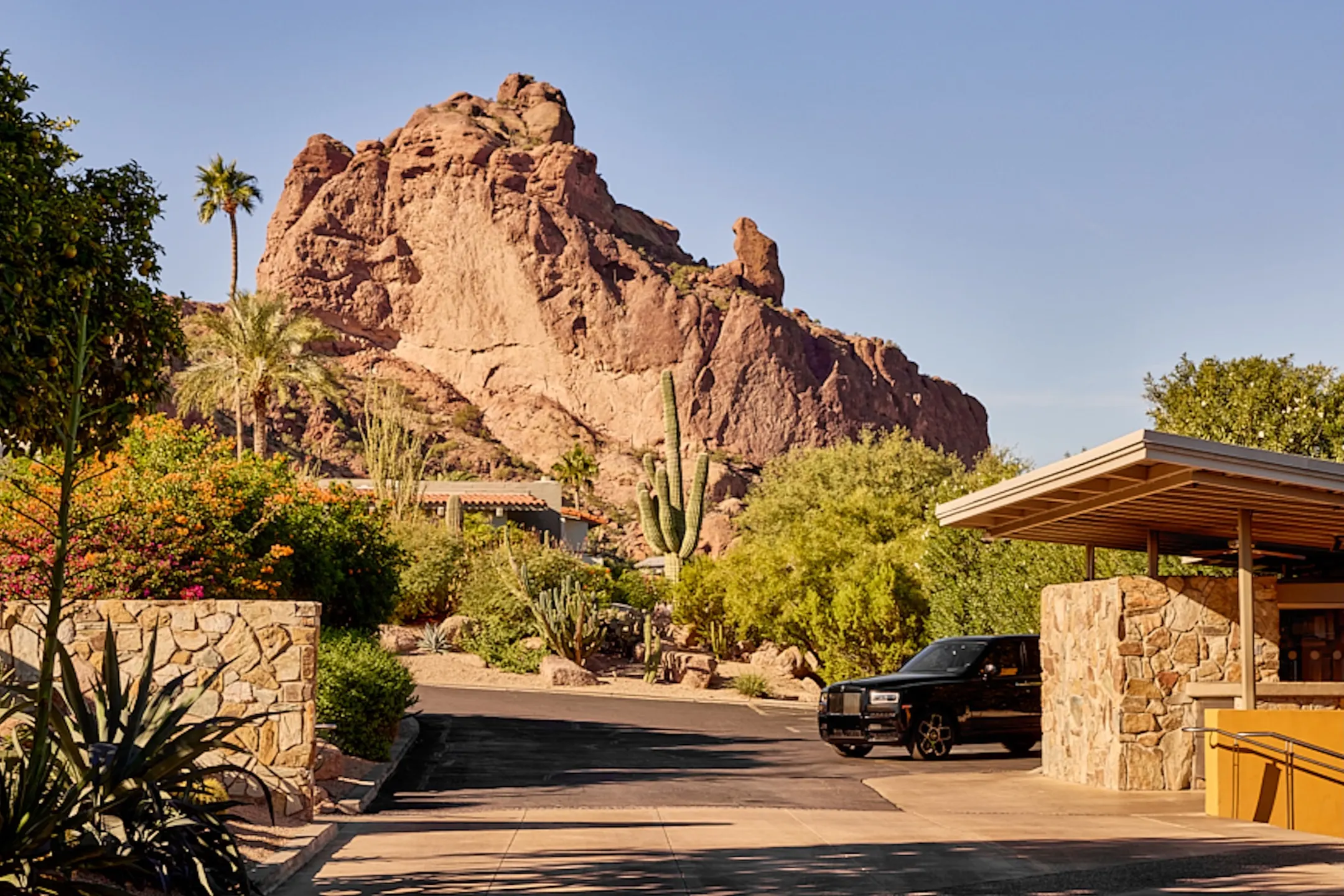 Main entrance of Sanctuary Camelback Mountain Resort surrounded by desert plants and a prominent rock formation in the background.
