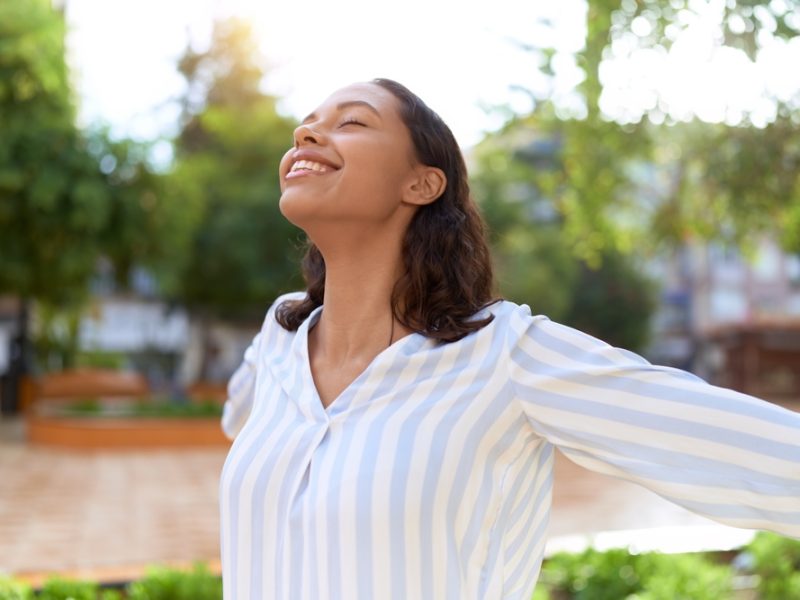 Woman with a joyful expression standing outdoors, enjoying the fresh air in a lush green park.
