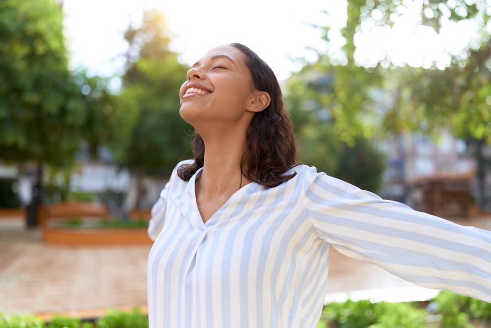 Woman with a joyful expression standing outdoors, enjoying the fresh air in a lush green park.