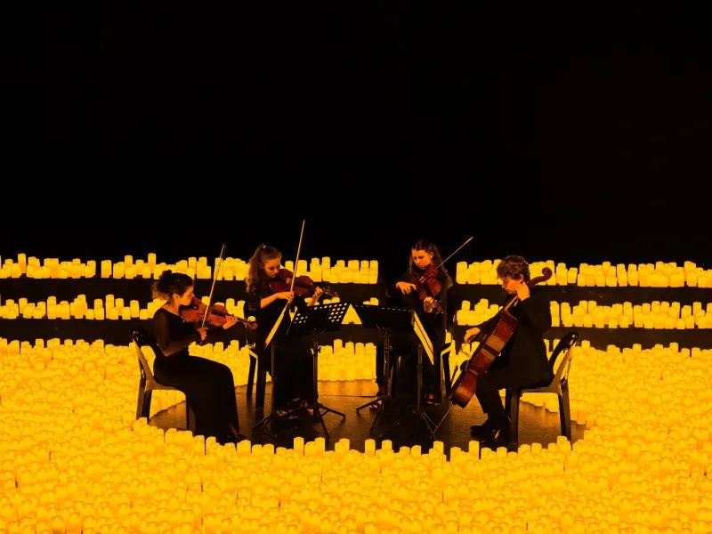 A string quartet performs surrounded by glowing candles, creating a serene atmosphere at a candlelight concert in Los Angeles.