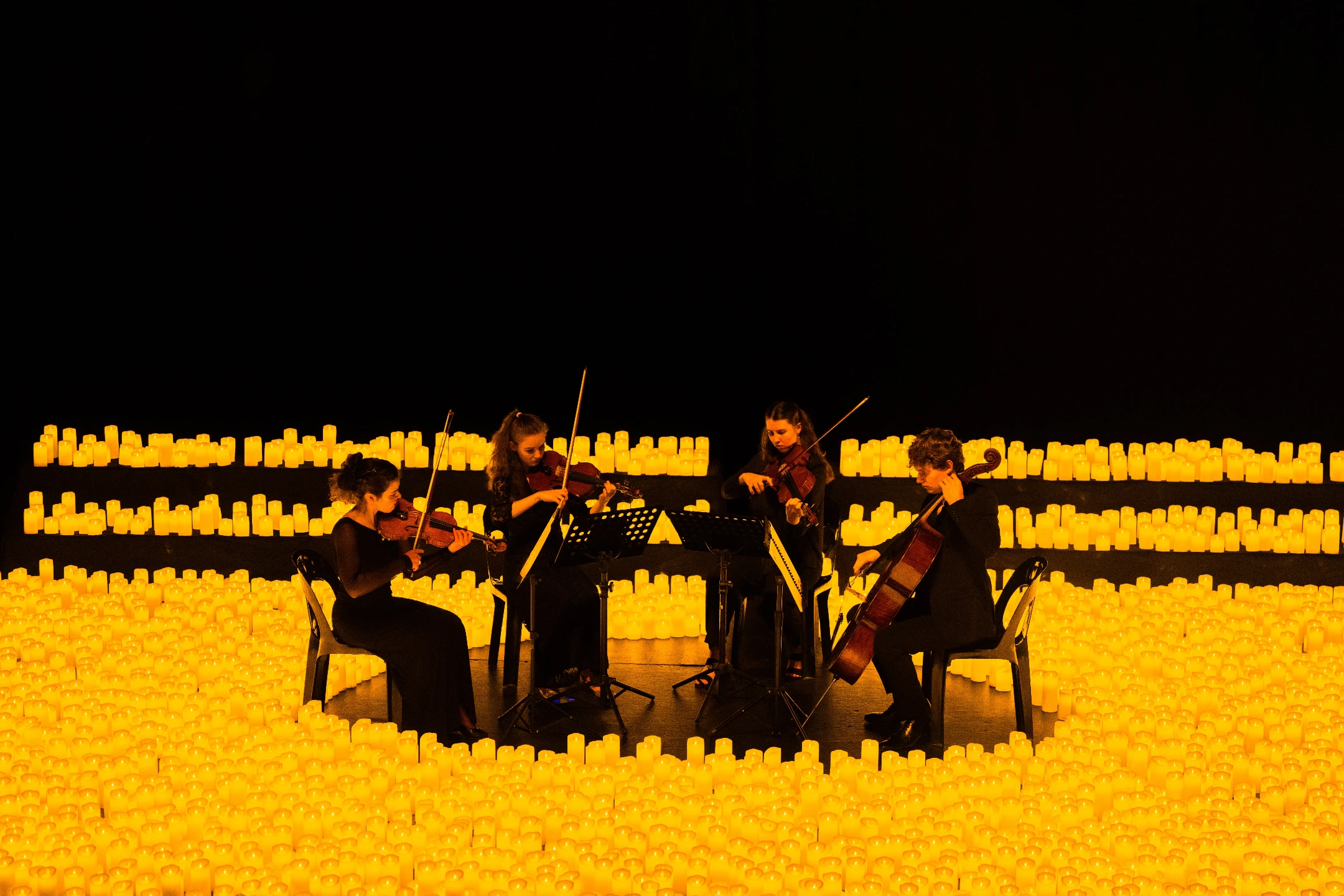 A string quartet performs surrounded by glowing candles, creating a serene atmosphere at a candlelight concert in Los Angeles.