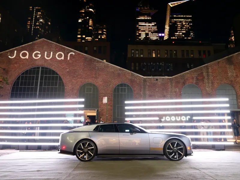 Jaguar's sleek new vehicle showcased in front of a brick building with neon lights during the Type 01 global reveal event.