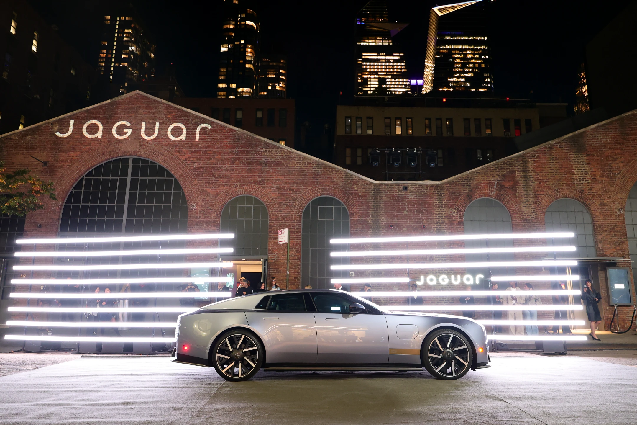 Jaguar's sleek new vehicle showcased in front of a brick building with neon lights during the Type 01 global reveal event.