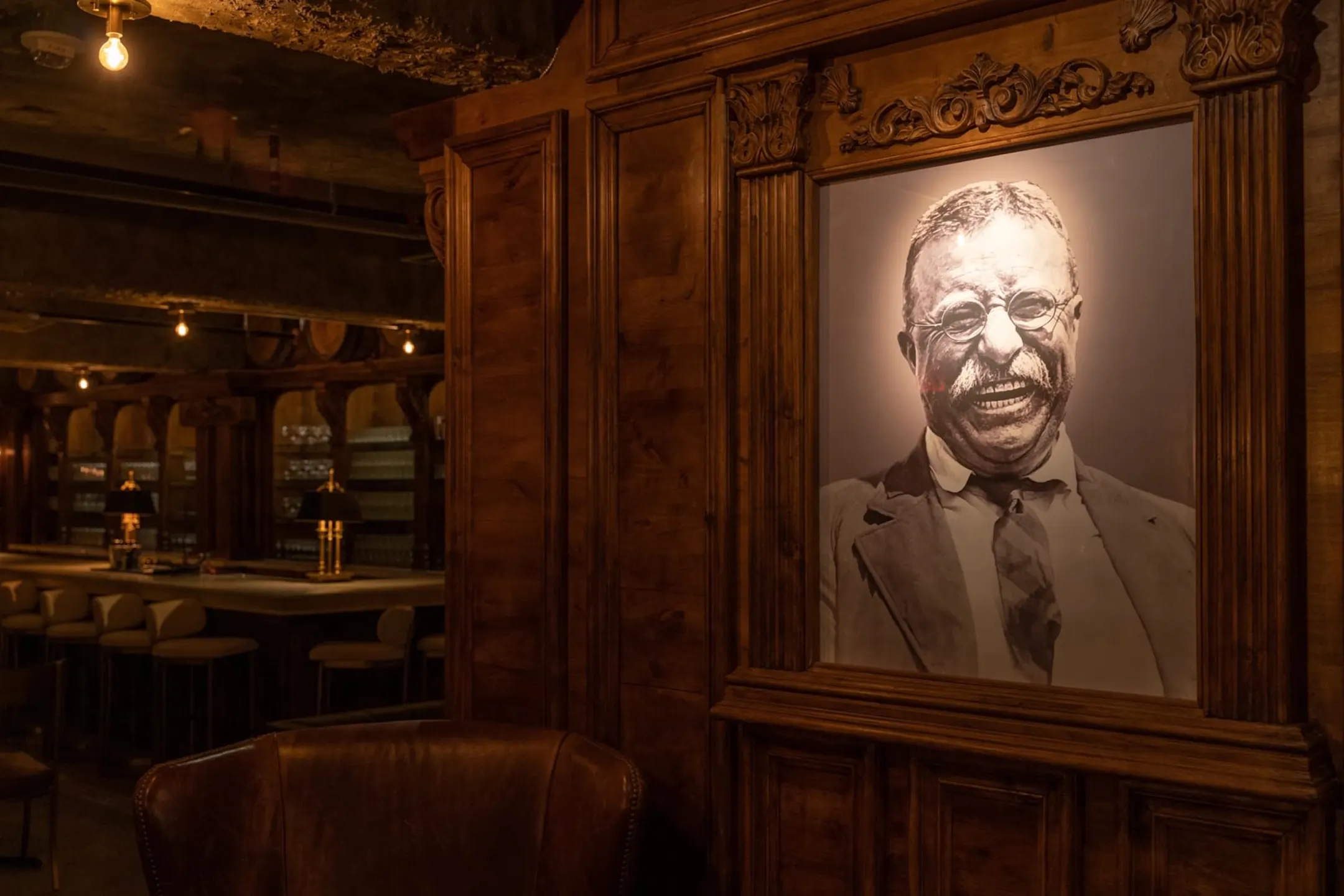 Framed portrait of Theodore Roosevelt in a cozy, wooden-panelled speakeasy setting with warm lighting.