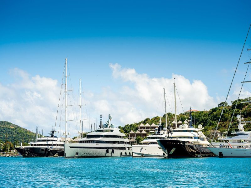 Several luxury superyachts docked at a marina under a clear blue sky, showcasing a picturesque summer scene in Italy.