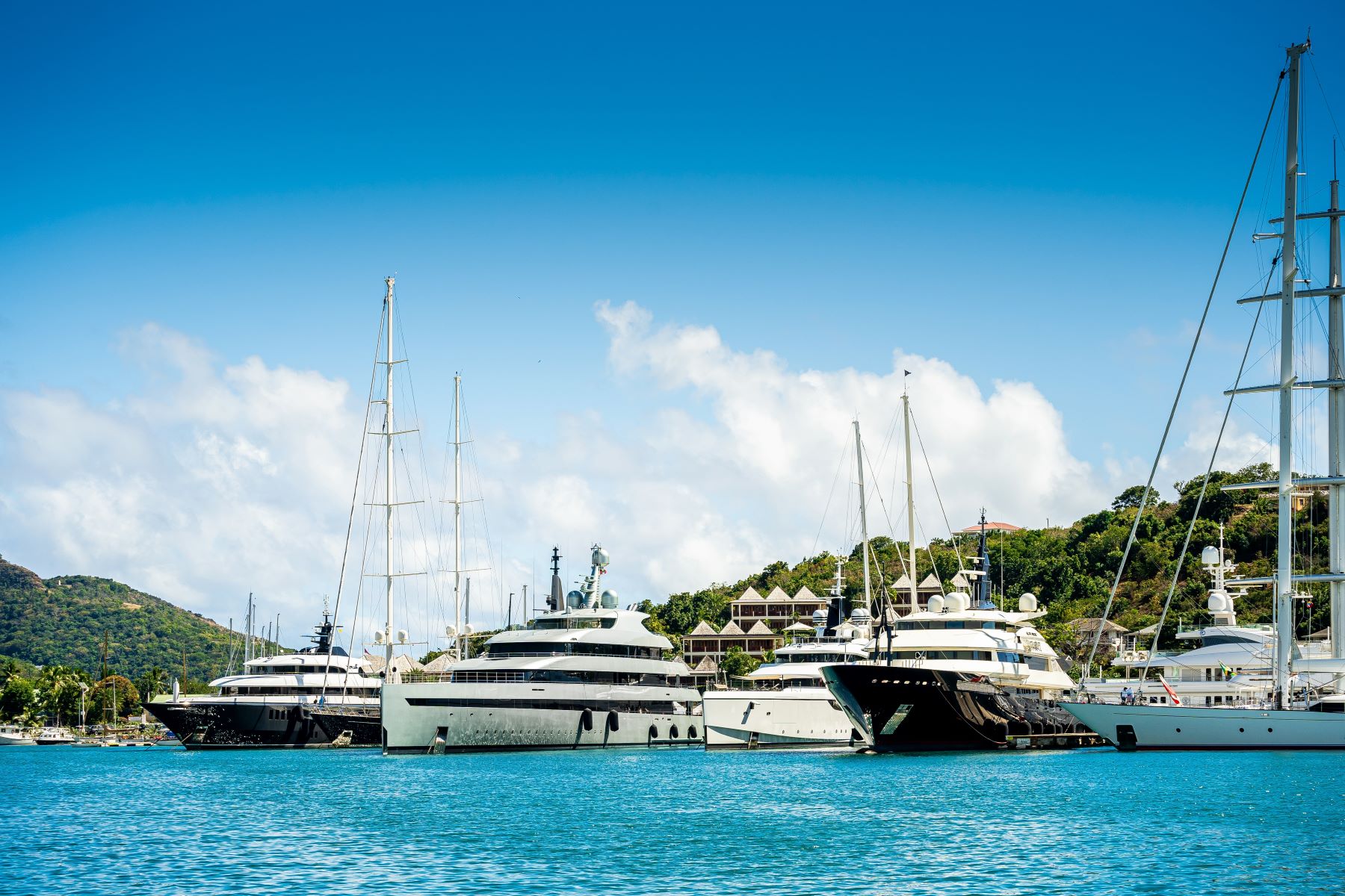 Several luxury superyachts docked at a marina under a clear blue sky, showcasing a picturesque summer scene in Italy.
