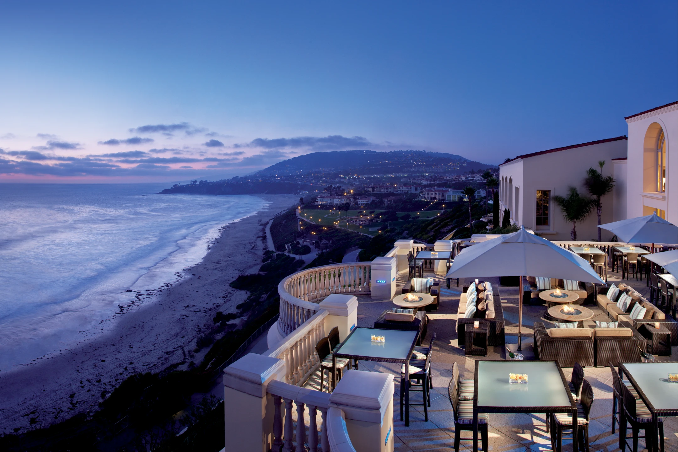 Views of the ocean from the terrace of The Ritz-Carlton, Laguna Niguel, with seating and glowing lights at dusk.