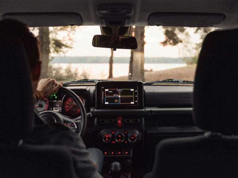 View from inside a car, showing the driver’s hands on the steering wheel and a digital display with navigation features.