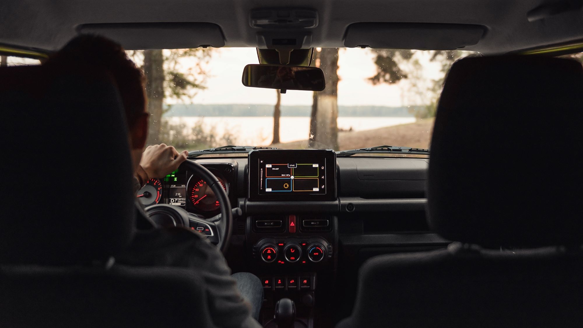 View from inside a car, showing the driver’s hands on the steering wheel and a digital display with navigation features.
